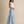 A woman modeling a light blue and white patterned tiered maxi skirt with a white short-sleeve top, standing against a neutral beige studio backdrop.