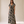 A woman modeling a black and beige palm leaf print maxi dress with short flutter sleeves, a V-neckline, and a tie detail at the waist, standing against a neutral beige studio backdrop.