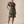 A woman modeling a short-sleeve button-front shirt dress with an abstract watercolor-style print in teal, olive green, mustard, and brown tones, paired with brown strappy sandals against a warm beige studio backdrop.