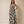 A woman modeling a sleeveless maxi dress with a black and off-white floral print, featuring a V-neckline, waist tie, and a high side slit, set against a plain beige studio backdrop.