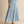 A woman modeling a white short-sleeve crewneck t-shirt and a high-waisted, tiered light blue maxi skirt with a subtle vertical abstract pattern, paired with tan strappy sandals, against a solid beige studio backdrop.