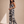 A woman modeling a sleeveless black jumpsuit with a large white floral print, standing against a textured beige studio backdrop.