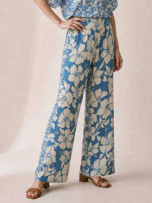 A woman modeling a blue and cream floral short-sleeve wrap top and matching wide-leg pants set, standing against a neutral beige studio backdrop.