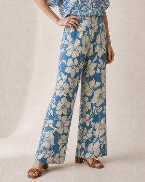 A woman modeling a blue and cream floral short-sleeve wrap top and matching wide-leg pants set, standing against a neutral beige studio backdrop.