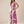 A woman modeling a sleeveless maxi dress with a bold purple tropical leaf pattern on a cream background, paired with tan flat sandals, against a solid beige studio backdrop.