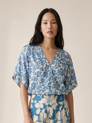A woman modeling a matching two-piece set featuring a blue and beige floral print, consisting of a short-sleeve V-neck top and wide-leg trousers, set against a plain beige studio background.