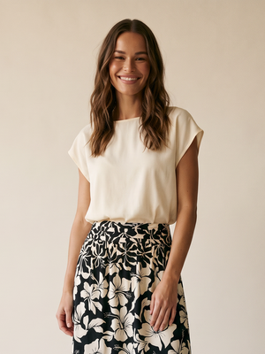 A woman modeling a cream short-sleeve top and a black midi skirt with a cream floral print, standing against a plain beige studio background.