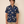 A man wearing a navy blue short-sleeve button-up shirt with a white and beige floral pattern, paired with khaki shorts, standing against a solid beige background.