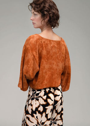 Woman wearing a rust-colored top and patterned pants on a gray background