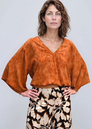 Woman wearing an orange top and patterned pants on a white background