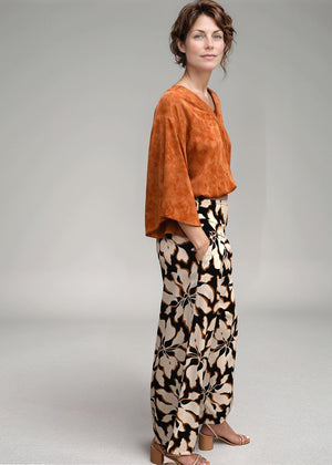 Woman wearing an orange top and patterned pants on a plain background