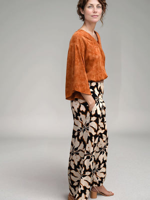 Woman wearing an orange top and patterned pants on a plain background