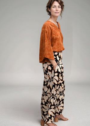 Woman wearing an orange top and patterned pants on a plain background